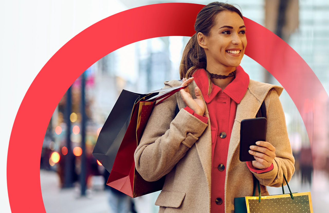 Smiling woman holding a cell phone with a shopping bag over her shoulder, symbolizing a satisfied shopper using mobile shopping solutions.