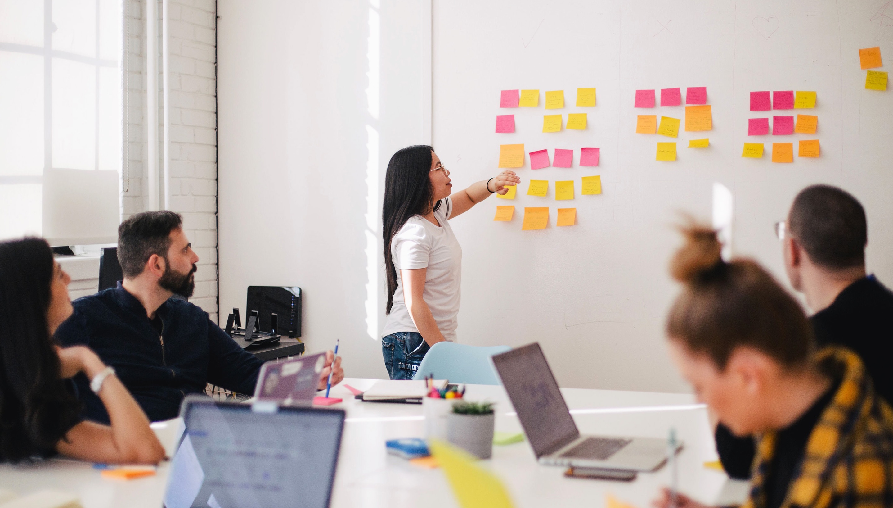 woman reading off sticky notes from wall to team members