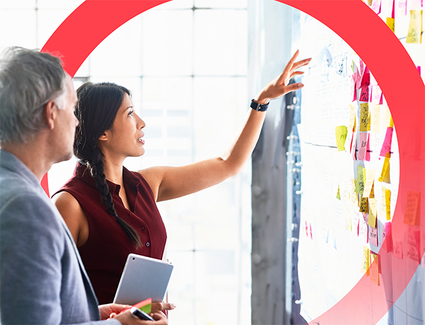 woman pointing at a board with notes and speaking to a colleague