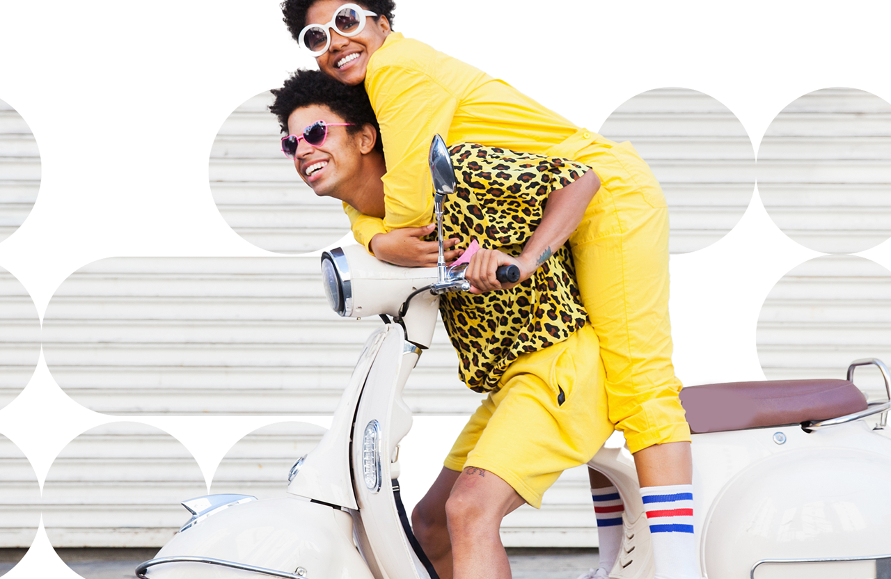 Two people, both dressed in yellow and wearing sunglasses, riding a white motor scooter, against a background of geometric shapes.