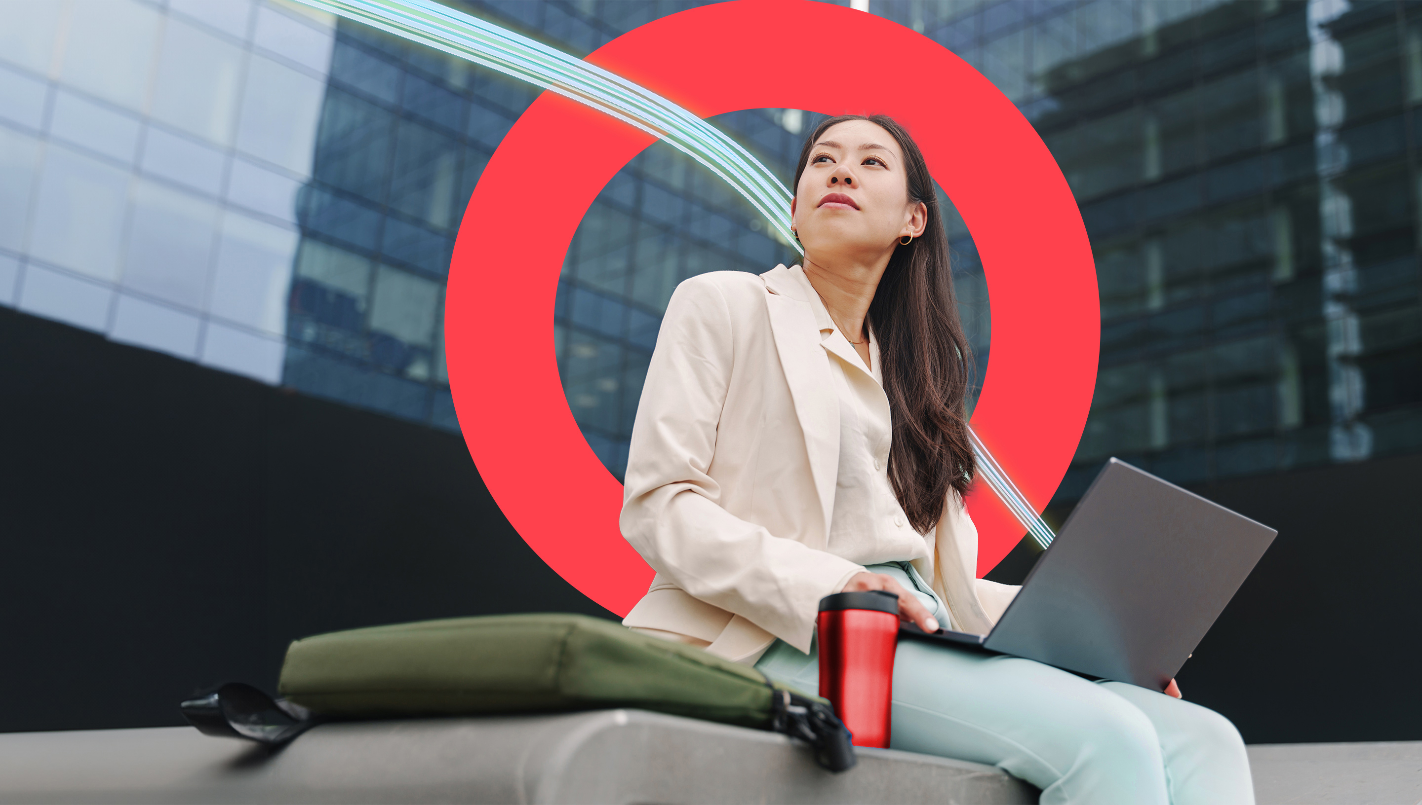 A businesswoman works on her laptop while sitting on a bench in front of her office building.